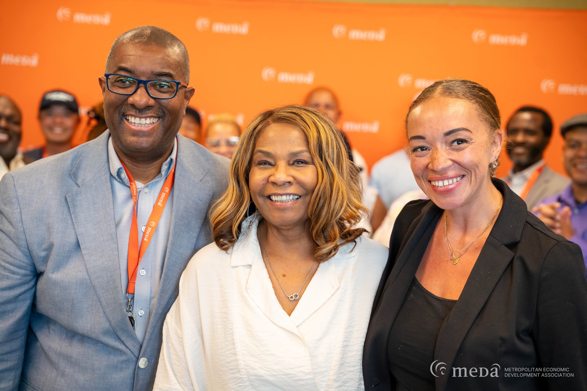 Alivia Boddie with two MEDA colleagues in front of an orange MEDA backdrop