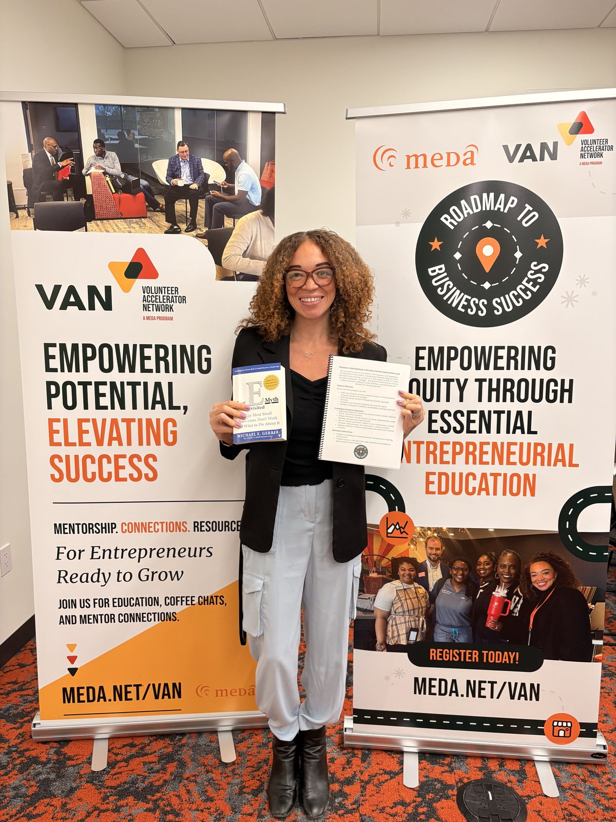 Alivia Boddie holding The E-Myth beside MEDA, VAN, and Roadmap to Business Success banners